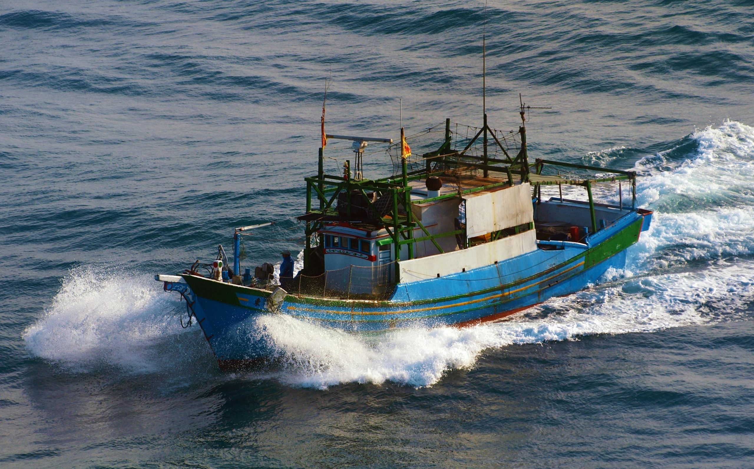 A vibrant fishing boat cuts through ocean waves off the coast of Taiwan, showcasing maritime life.